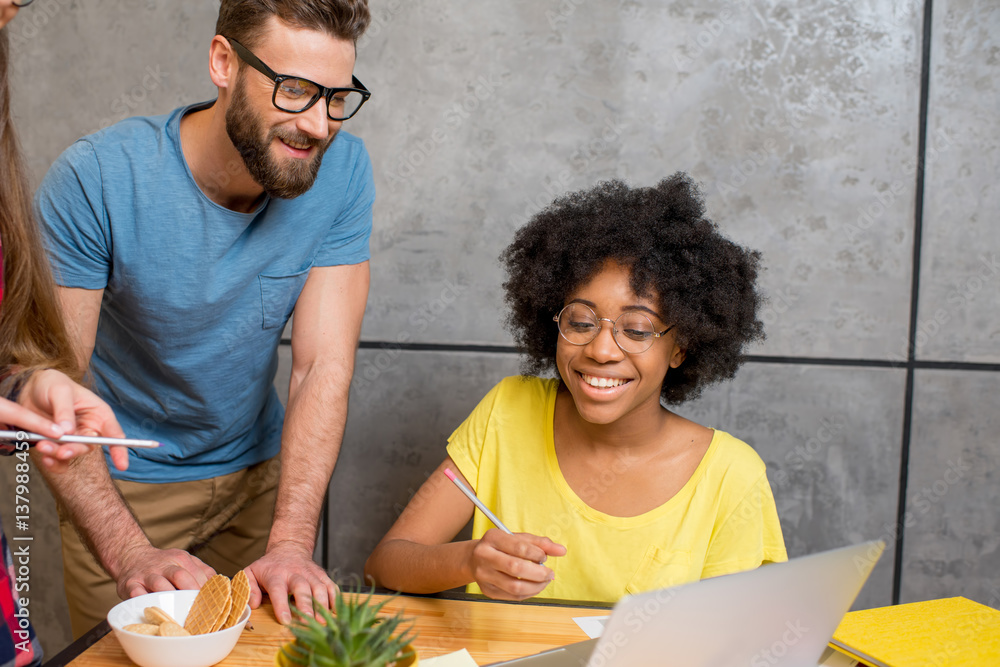 Multi ethnic coworkers dressed casually in colorful clothes talking together sitting with laptop ind