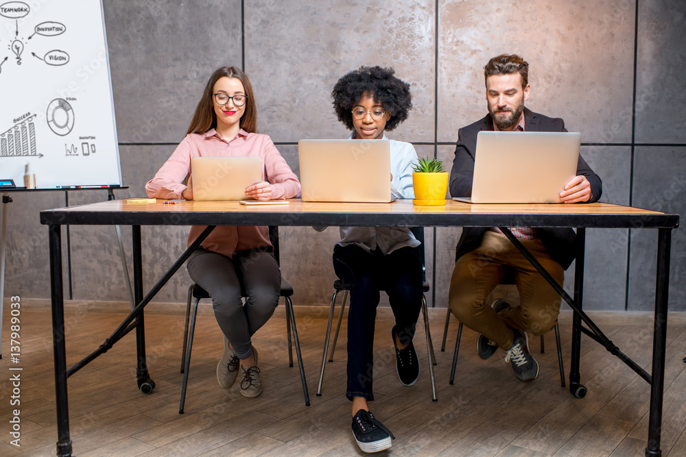 Multi ethnic coworkers working together with laptops and whiteboard at the modern office interior on