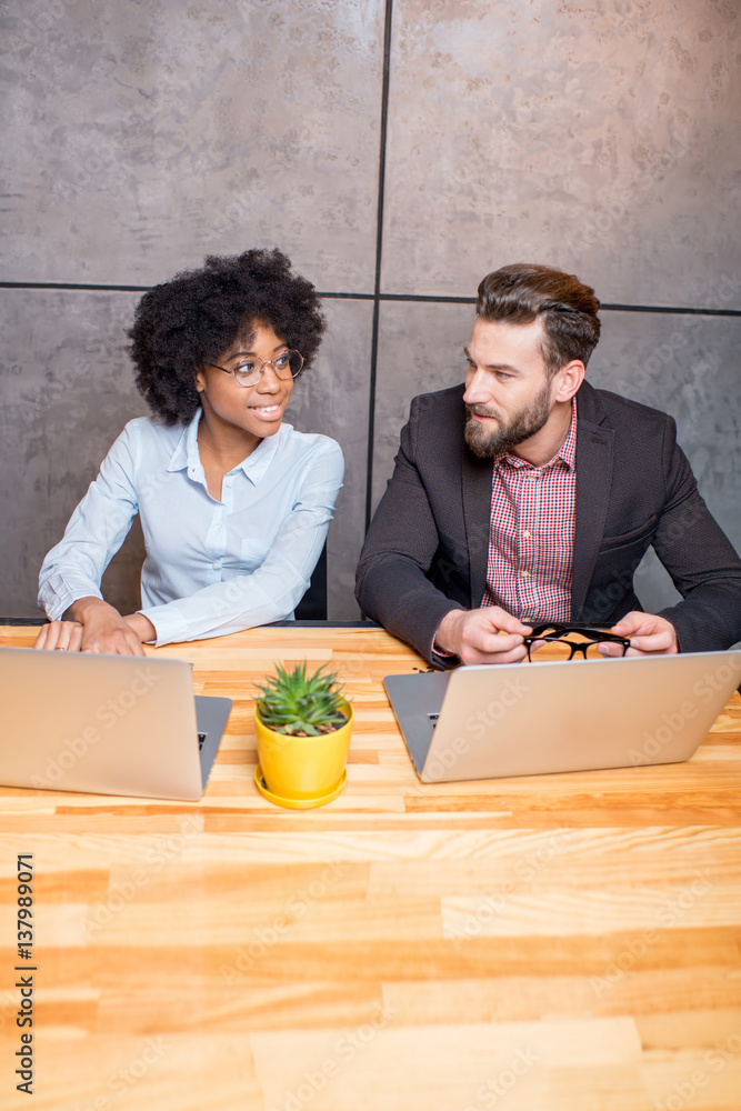 Beautiful african woman with handsome caucasian man working with laptop at the modern office interio