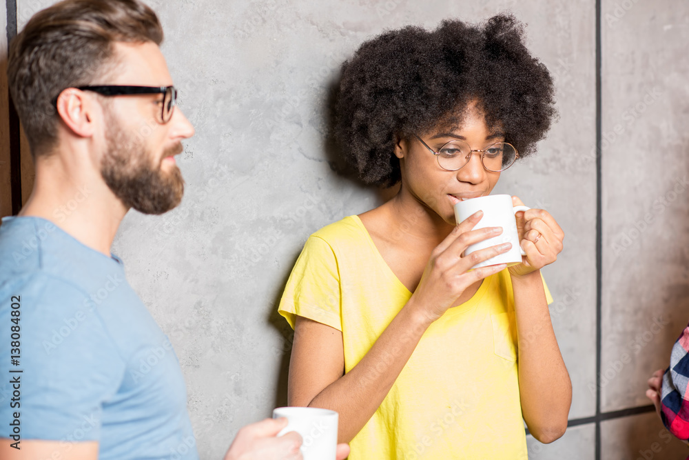 Multi ethnic coworkers dressed casually having a coffee break near the gray wall indoors