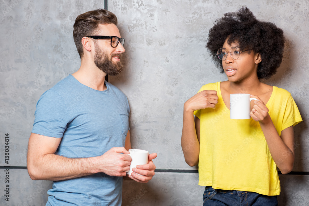 Multi ethnic coworkers dressed casually having a coffee break near the gray wall indoors