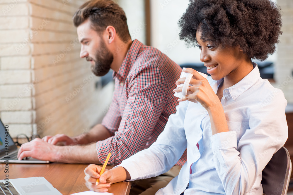 Beautiful african businesswoman and caucasian man working together with laptops and coffee cups near