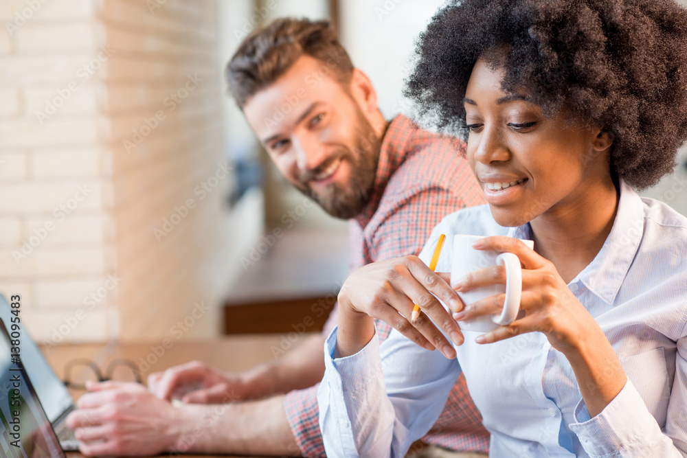 Beautiful african businesswoman and caucasian man working together with laptops and coffee cups near