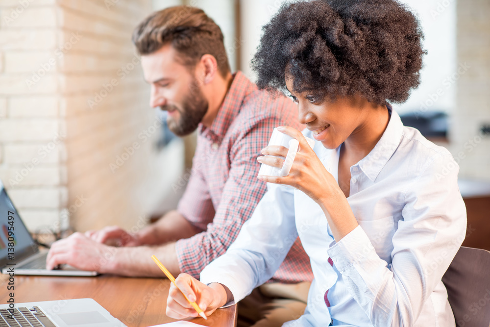 Beautiful african businesswoman and caucasian man working together with laptops and coffee cups near