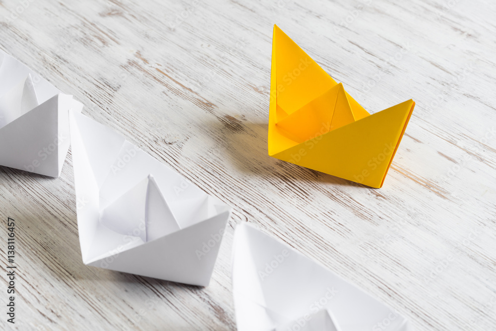 Business leadership concept with white and color paper boats on wooden table