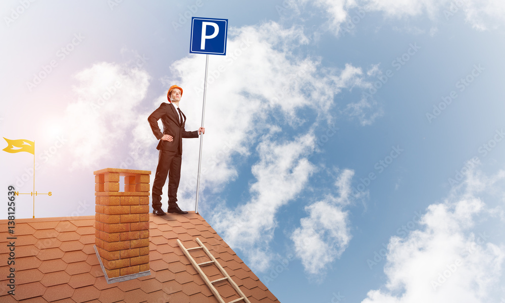 Young businessman with parking sign standing on brick roof. Mixed media