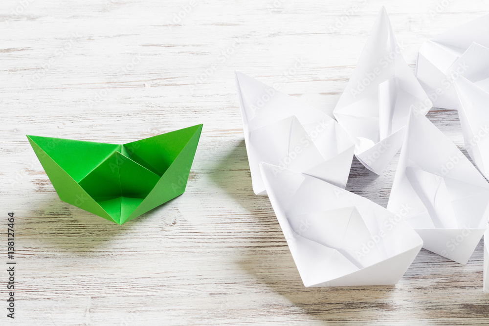 Business leadership concept with white and color paper boats on wooden table