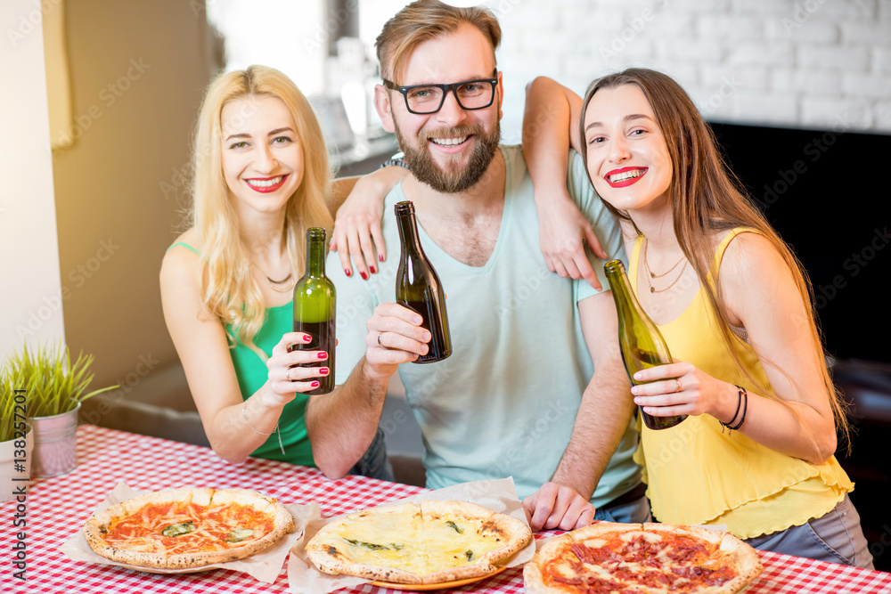 Portrait of the young friends dressed casually in colorful t-shirts having lunch with pizza and beer