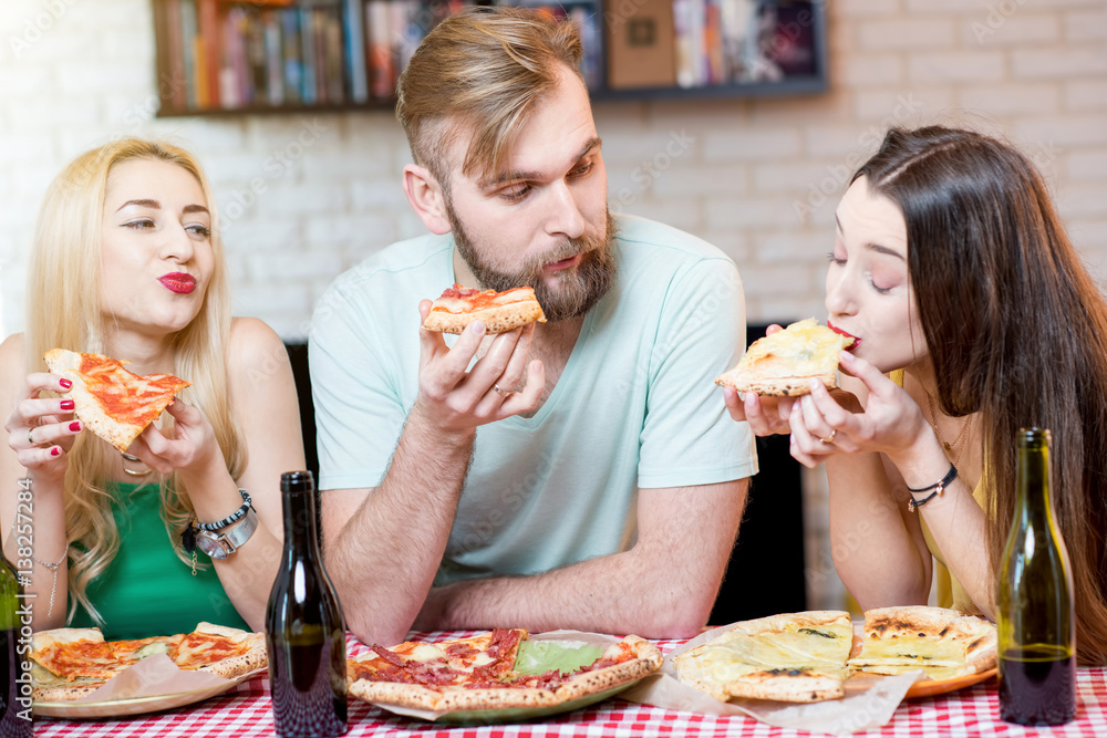 Young friends dressed casually in colorful t-shirts having lunch with pizza and beer at home