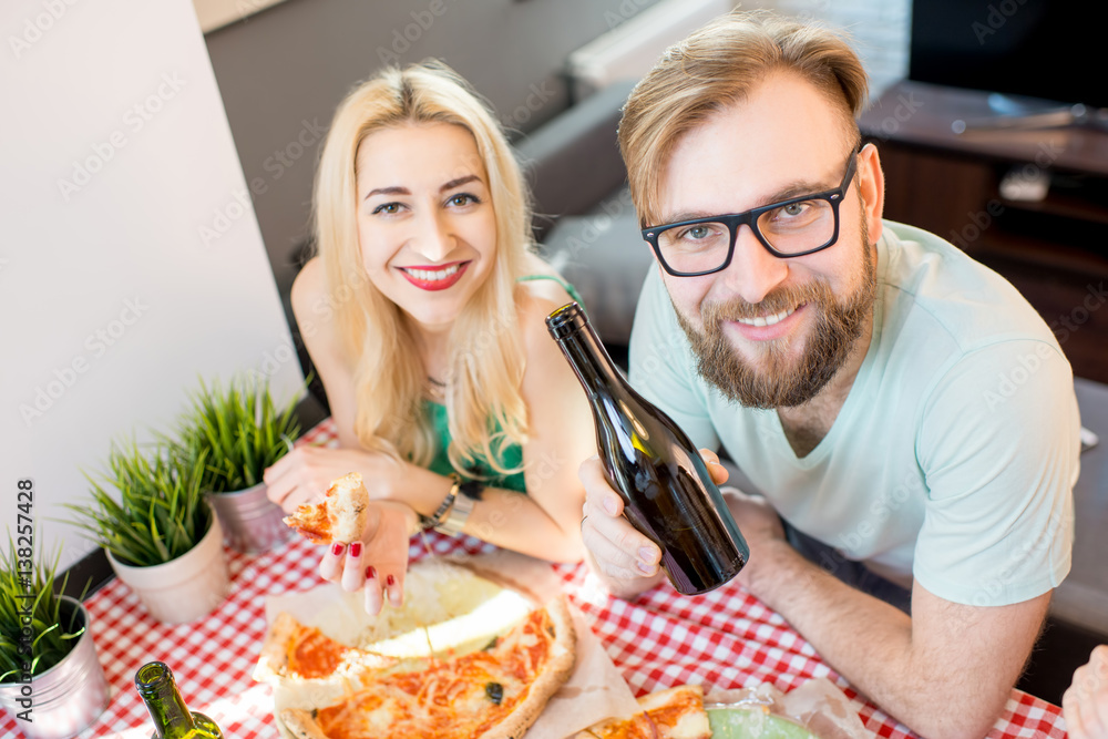 Young friends dressed casually in colorful t-shirts having lunch with pizza and beer at home