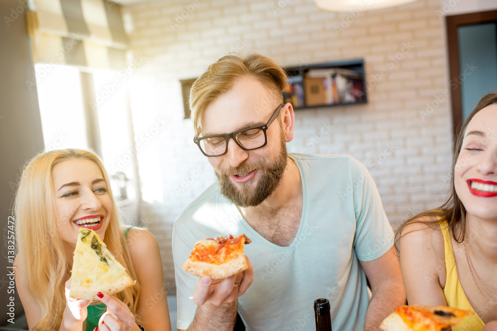 Young friends dressed casually in colorful t-shirts having fun eating pizza at home