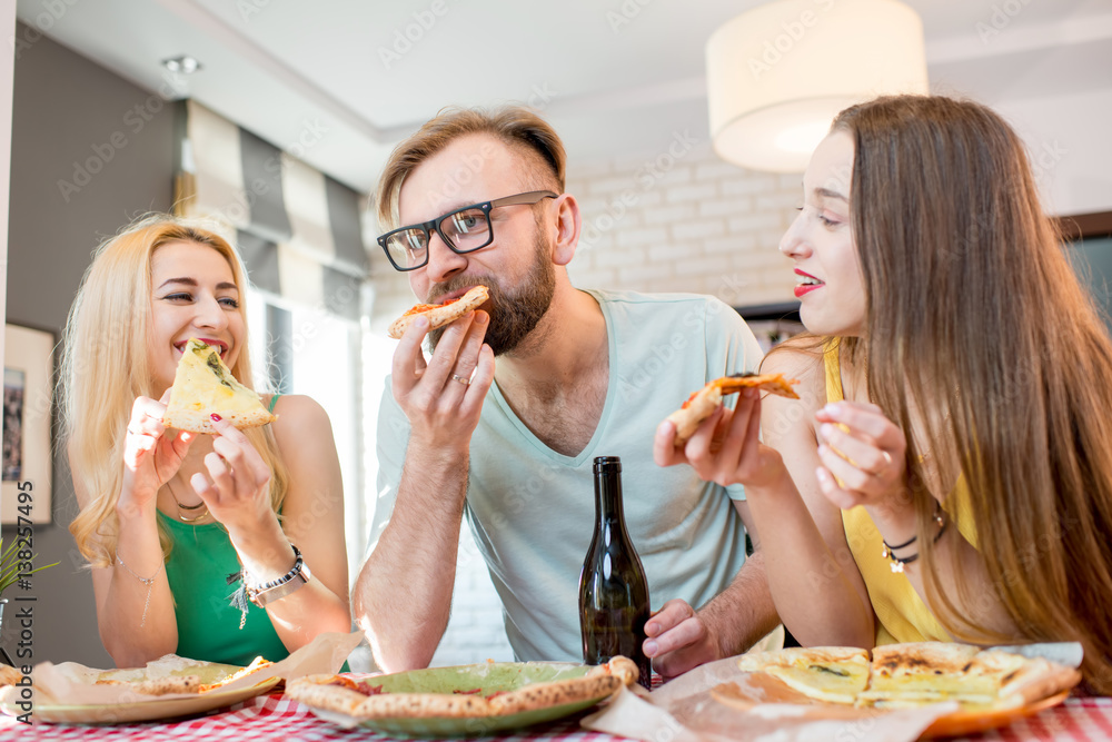 Young friends dressed casually in colorful t-shirts having lunch with pizza and beer at home