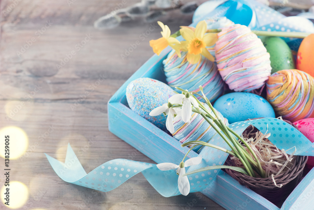 Easter colorful painted eggs with spring flowers and blue satin ribbon on wooden table top backgroun