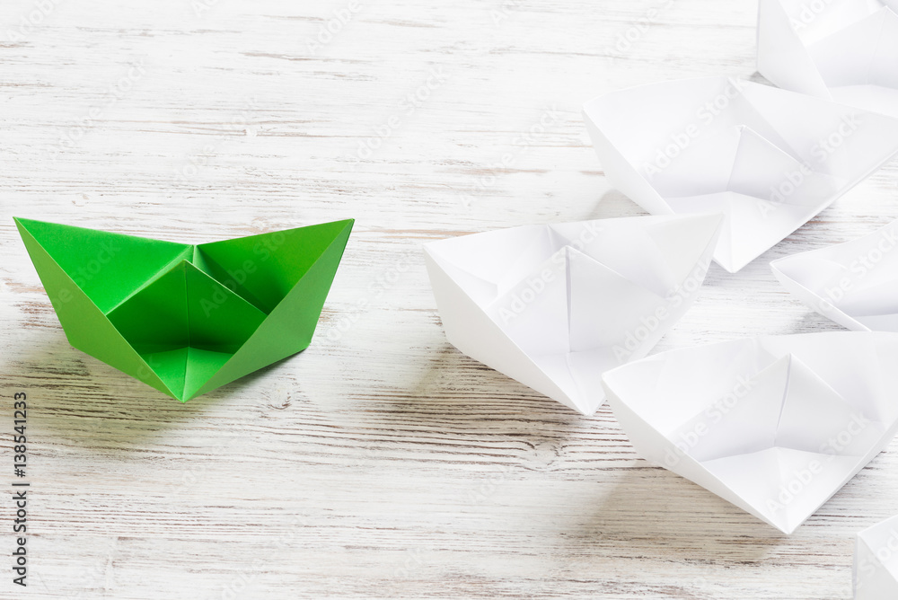 Business leadership concept with white and color paper boats on wooden table