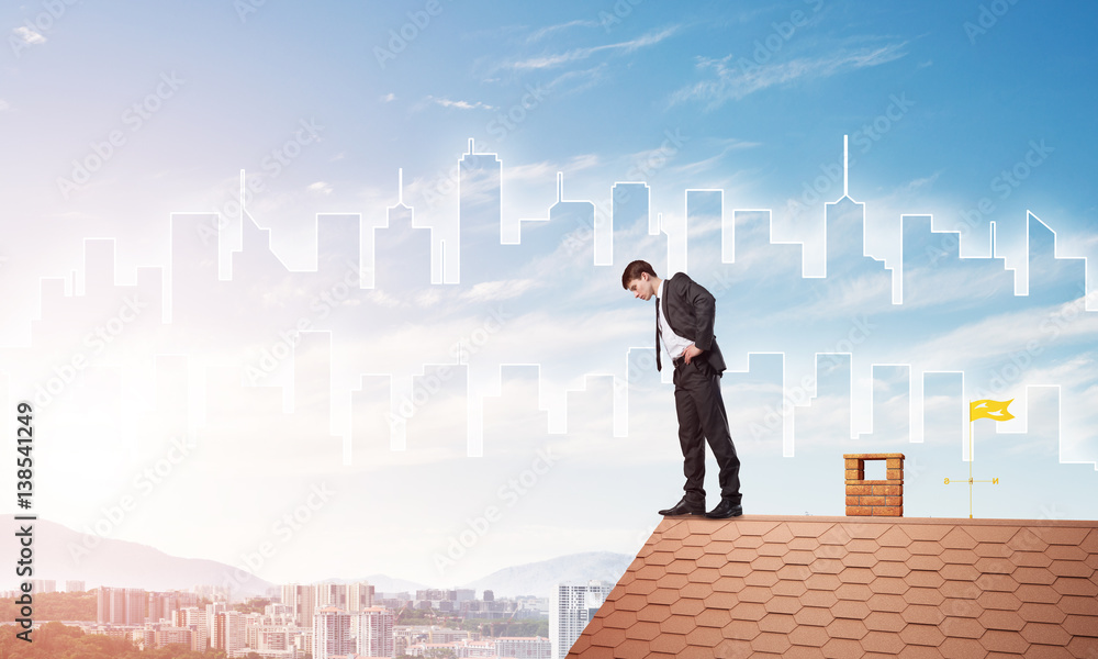 Businessman looking down from roof and modern cityscape at background. Mixed media