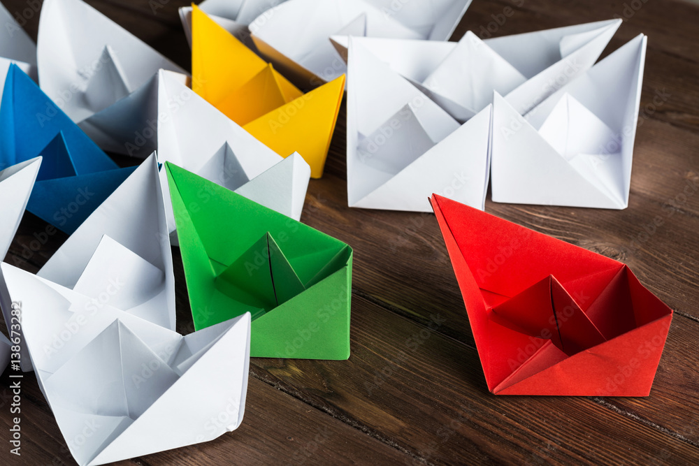 Business leadership concept with white and color paper boats on wooden table