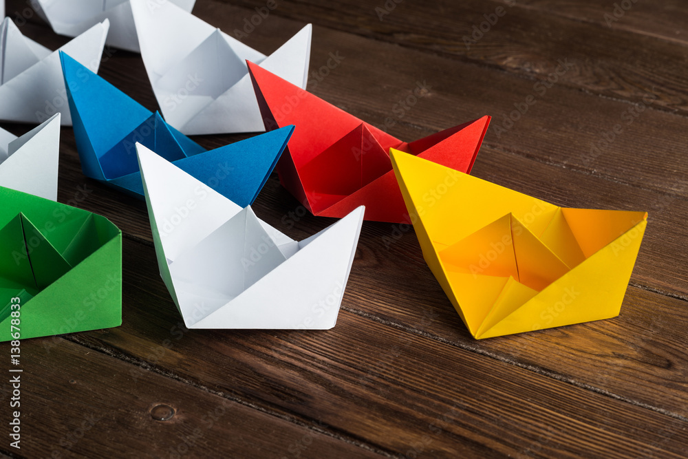 Business leadership concept with white and color paper boats on wooden table