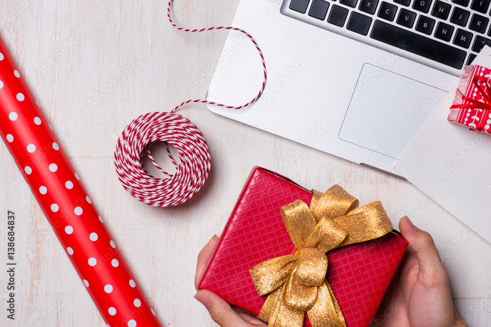 Male hands are holding a gift after wrapping near laptop on white wooden background