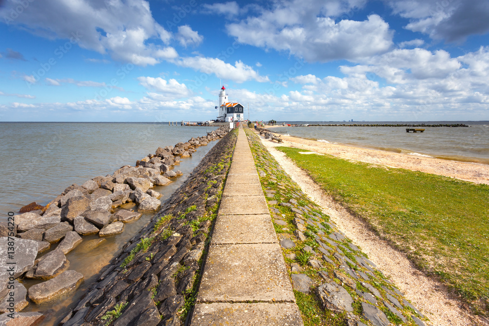 Stone path leading to the lighthouse on the sea coast on the background of blue sky with clouds at s