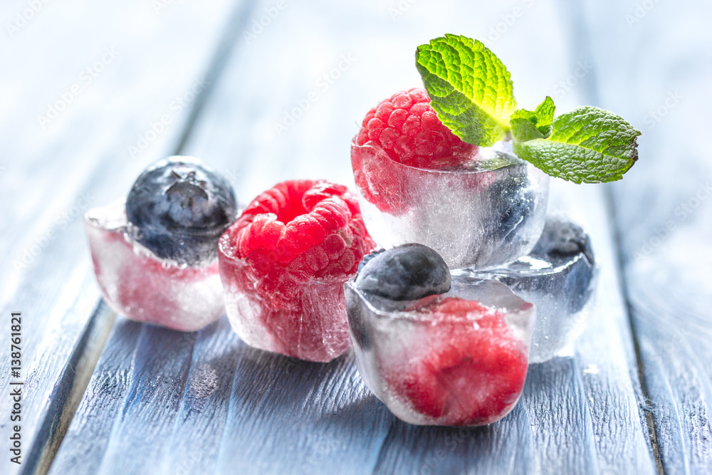 fresh berries with mint in ice cubes on wooden background