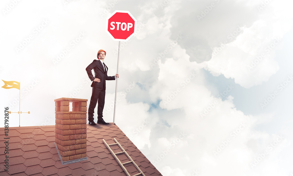 Caucasian businessman on brick house roof showing stop road sign