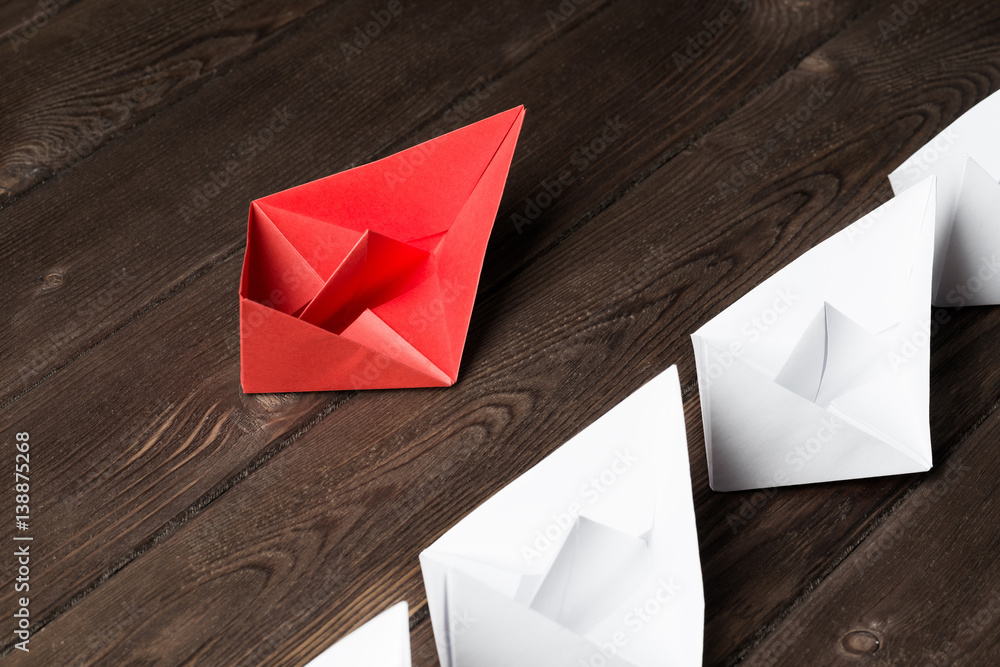 Business leadership concept with white and color paper boats on wooden table