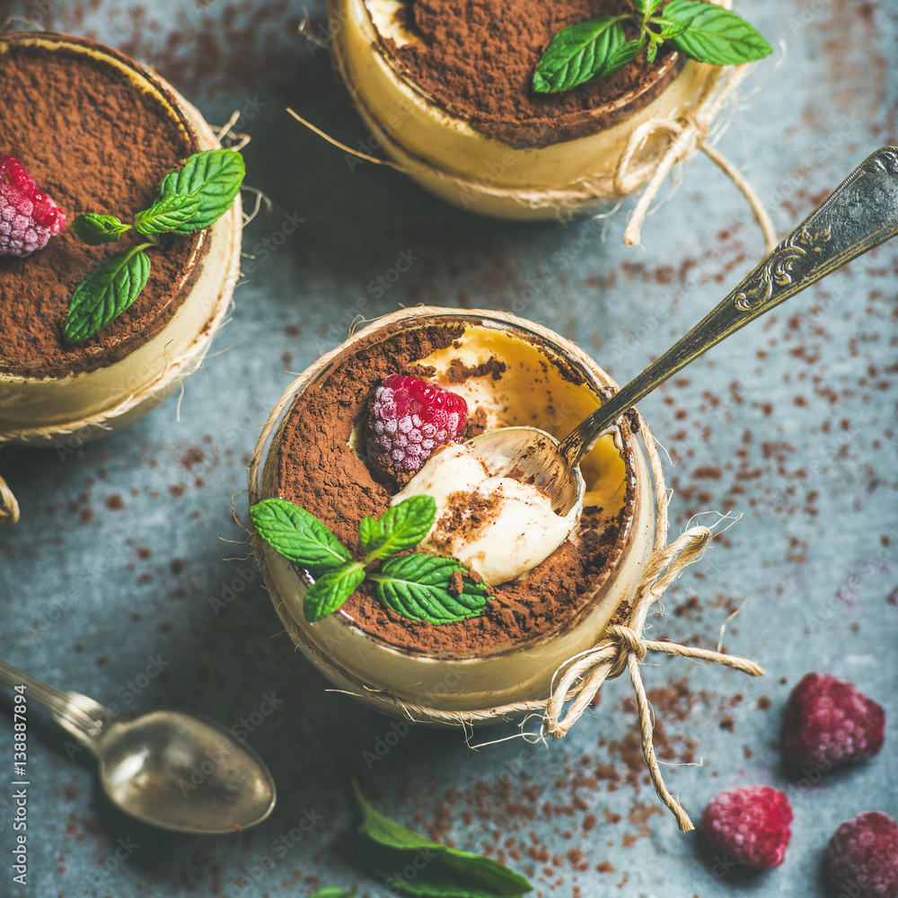 Close-up of homemade Italian dessert Tiramisu served in individual glasses with fresh mint leaves, r