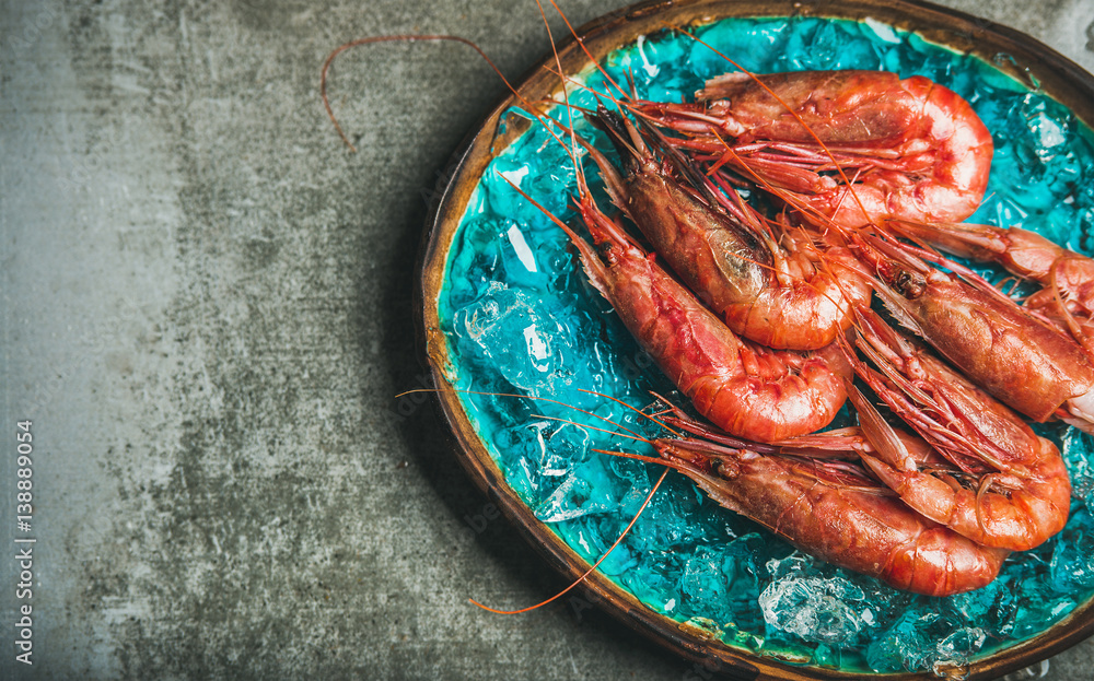 Raw uncooked red shrimps on chipped ice in turquoise blue ceramic tray over grey concrete background