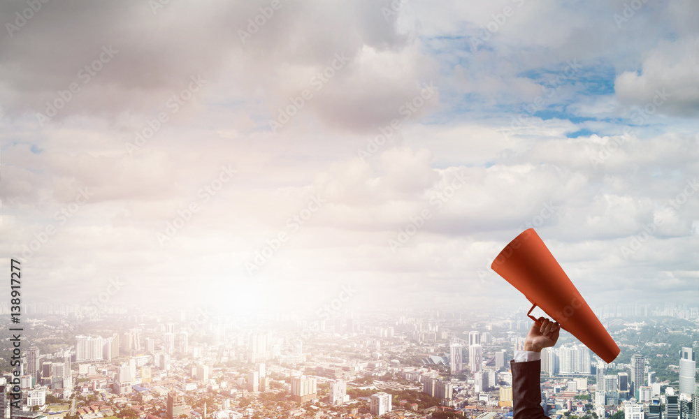 Hand of businesswoman holding red paper trumpet against cityscape background