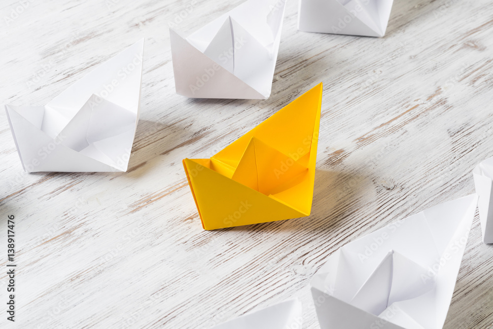 Business leadership concept with white and color paper boats on wooden table