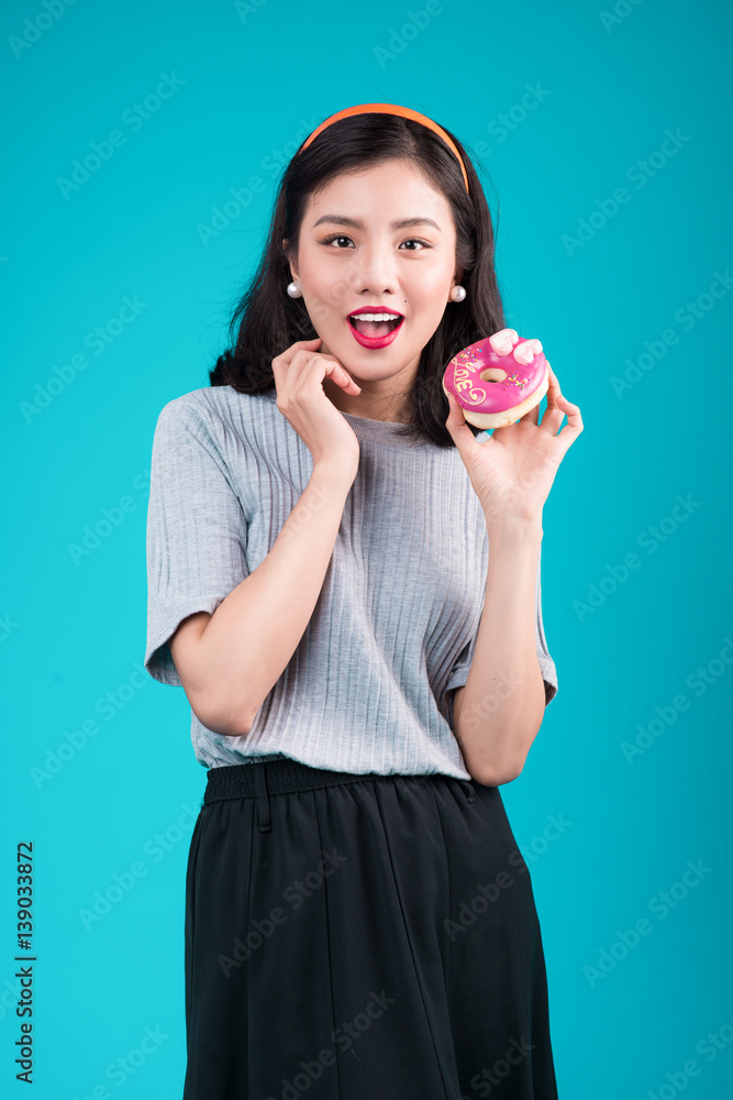 Asian beauty girl holding pink donut. Retro joyful woman with sweets, dessert standing over blue bac