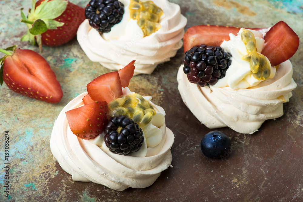 Mini Pavlova meringue cakes with berries and passion fruits on rustic vintage background. Top view.