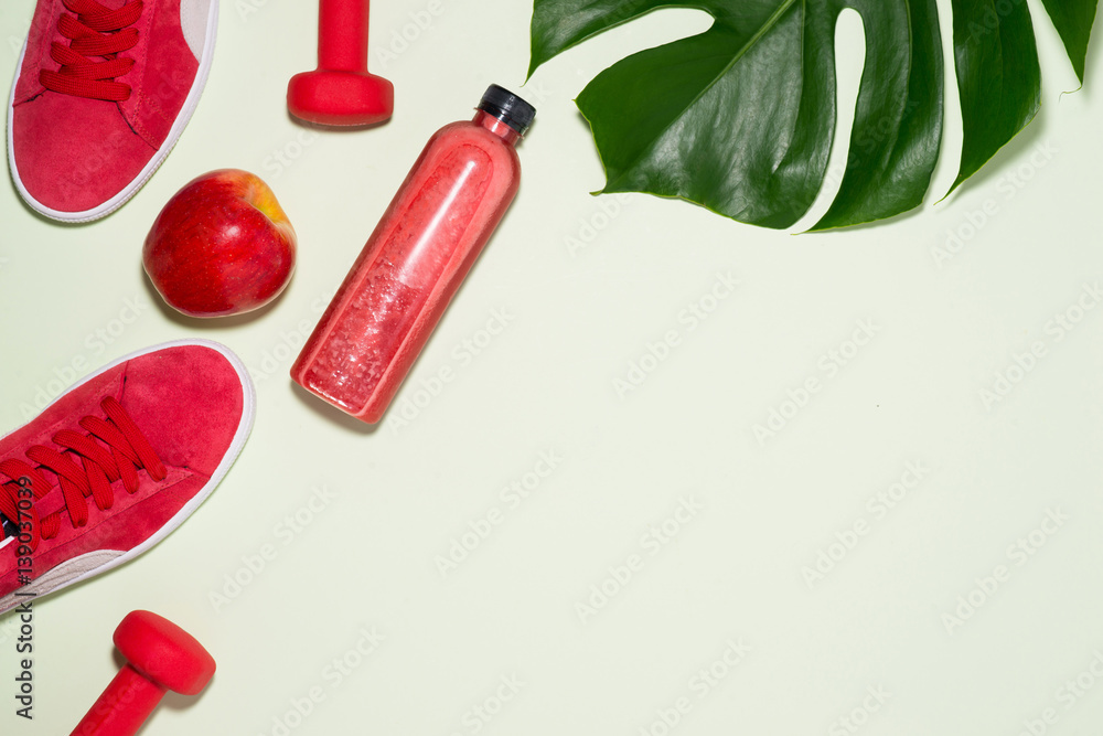 Fitness concept. Sneakers, apple, dumbbell and fruit juice bottle on pastel color background.