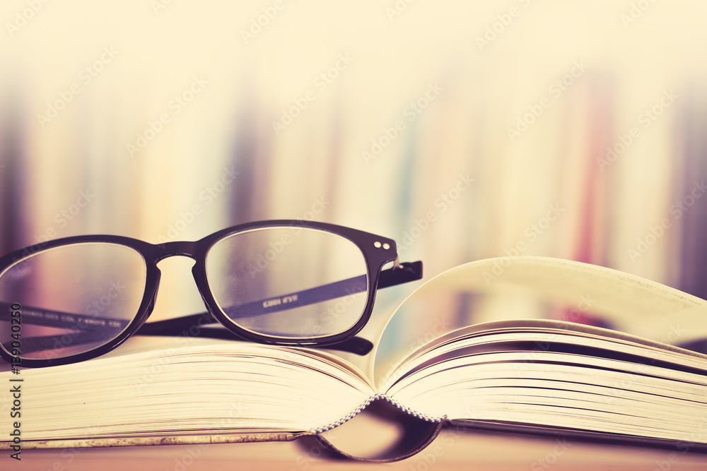 Close up opened book page and  reading eyeglasses with  blurry bookshelf background for education an