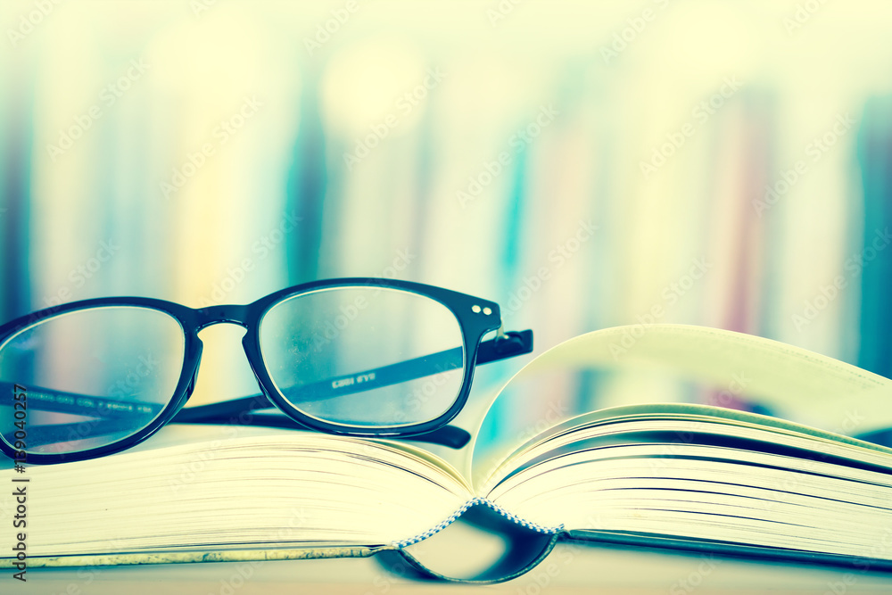 Close up opened book page and  reading eyeglasses with  blurry bookshelf background for education an