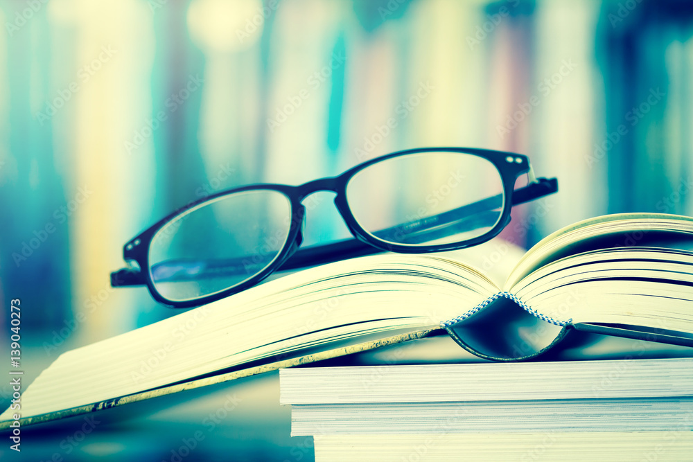 Close up opened book page and  reading eyeglasses with  blurry bookshelf background for education an