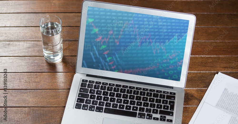 Laptop with document and glass of water on wooden table