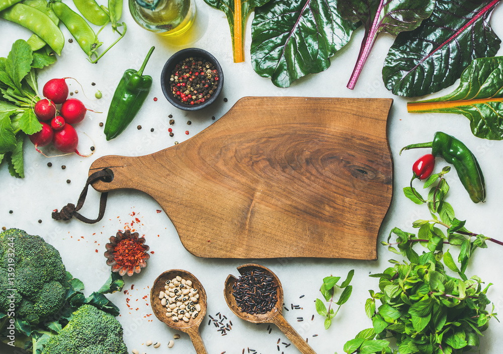 Fresh raw greens, unprocessed vegetables and grains over grey marble kitchen countertop, wooden boar