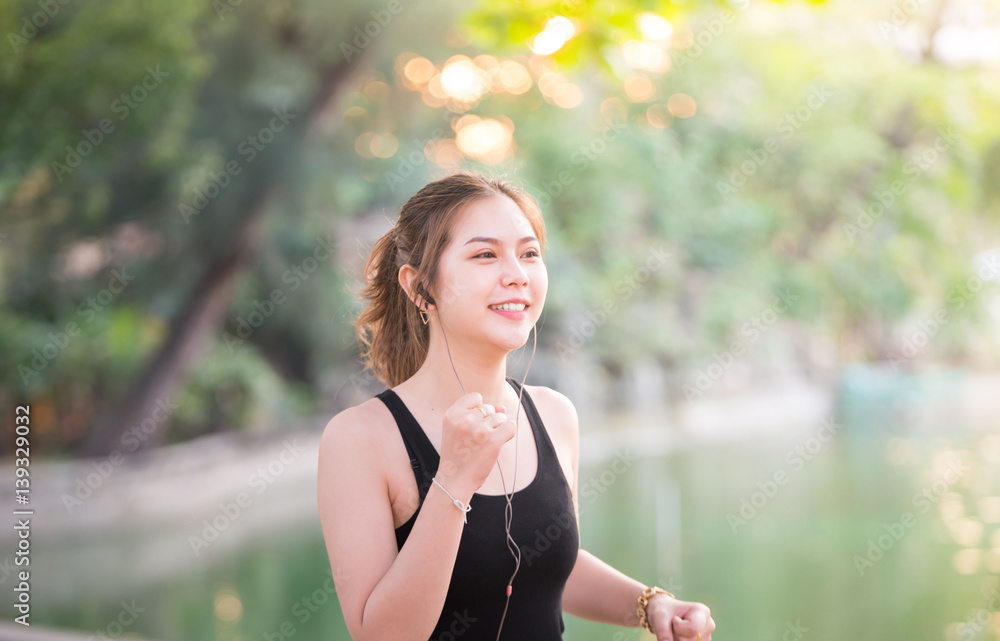 一名妇女在乡间小路上慢跑，一边用耳塞和MP3播放器听音乐。