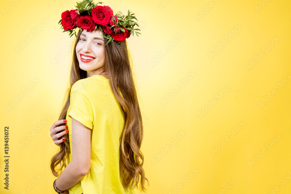 Colorful portrait of a beautiful woman in yellow t-shirt with wreath made of red roses on the yellow