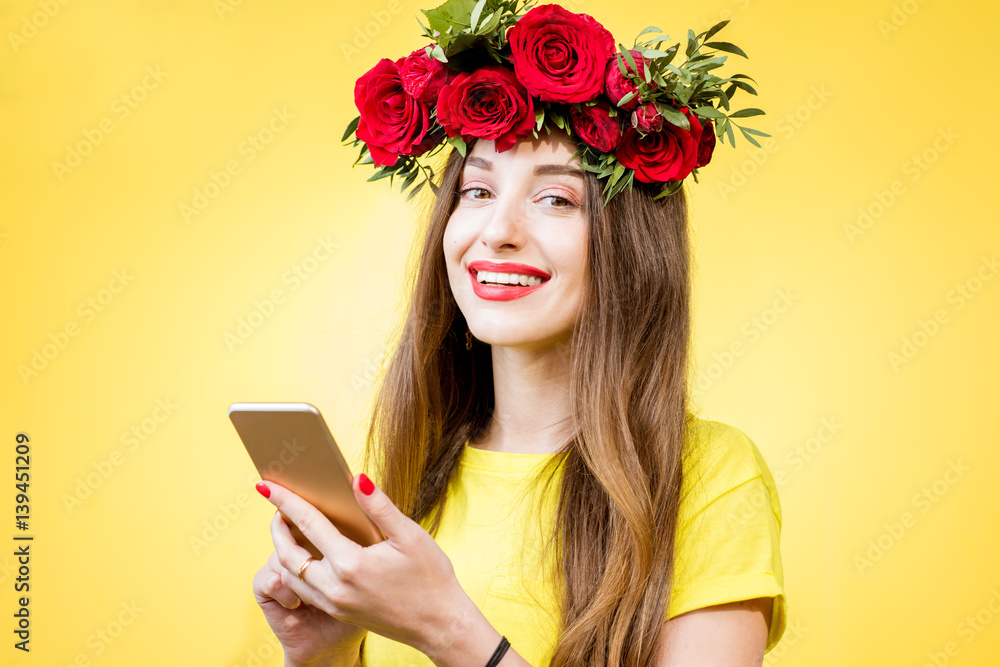 Colorful portrait of a beautiful woman in yellow t-shirt with wreath made of red roses using phone o