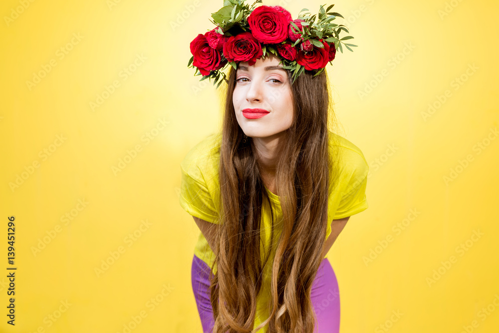 Colorful portrait of a beautiful woman in yellow t-shirt with wreath made of red roses on the yellow