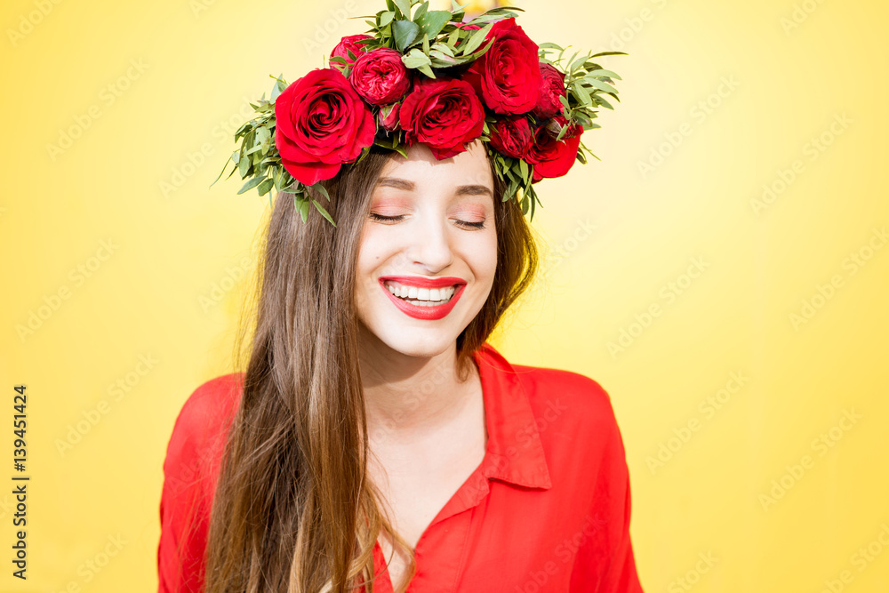 Colorful portrait of a beautiful woman in red dress with wreath made of red roses on the yellow back