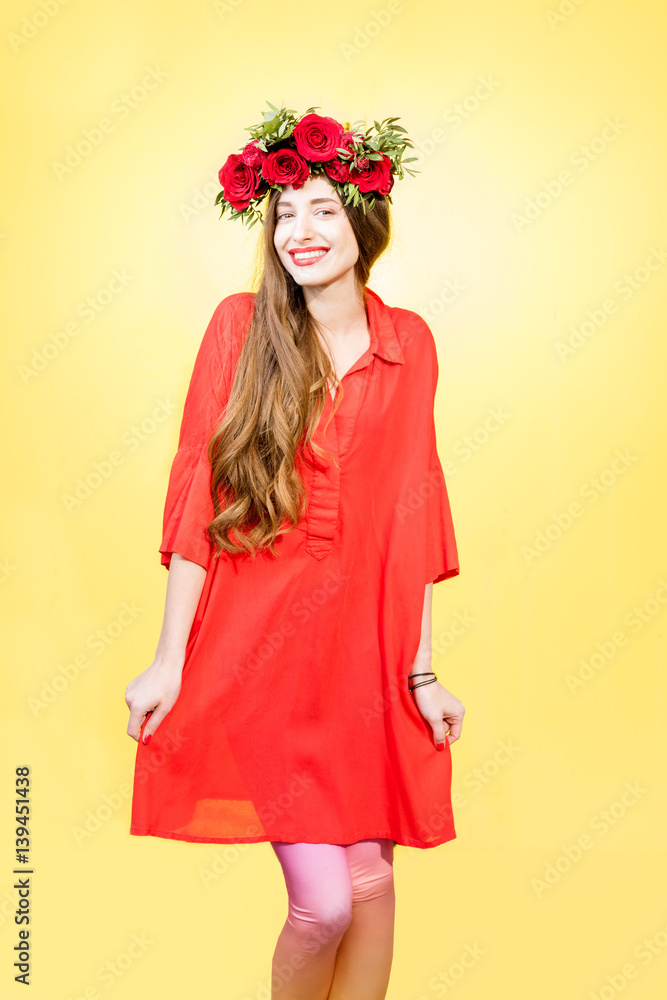 Colorful portrait of a beautiful woman in red dress with wreath made of red roses on the yellow back