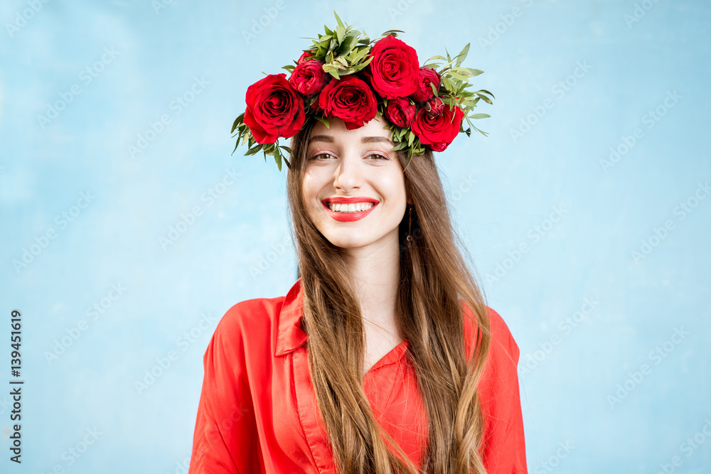 Colorful portrait of a beautiful woman in red dress with wreath made of red roses on the blue backgr