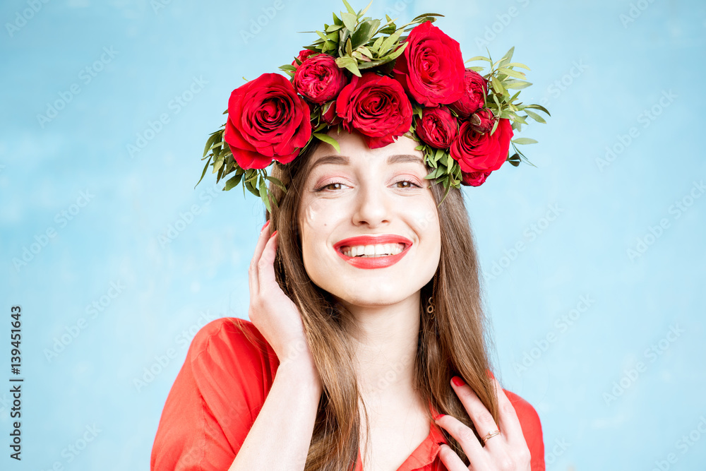 Colorful portrait of a beautiful woman in red dress with wreath made of red roses on the blue backgr