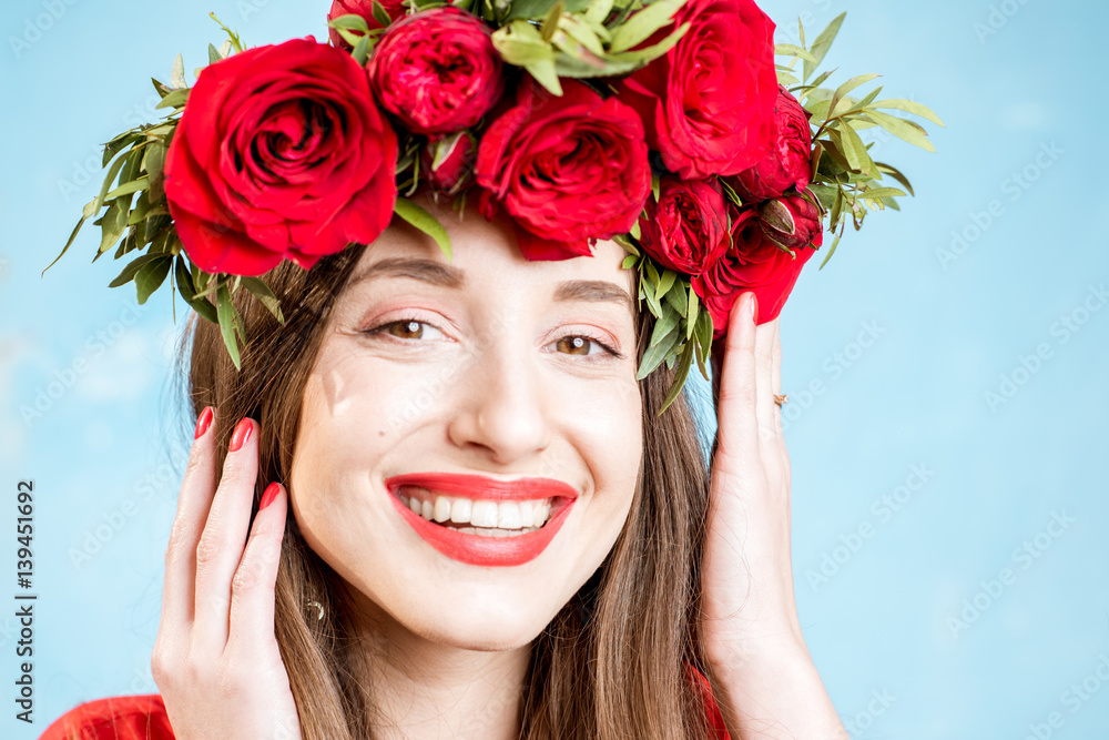 Colorful portrait of a beautiful woman in red dress with wreath made of red roses on the blue backgr