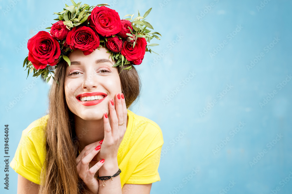 Colorful portrait of a beautiful woman in yellow t-shirt with wreath made of red roses on the blue b