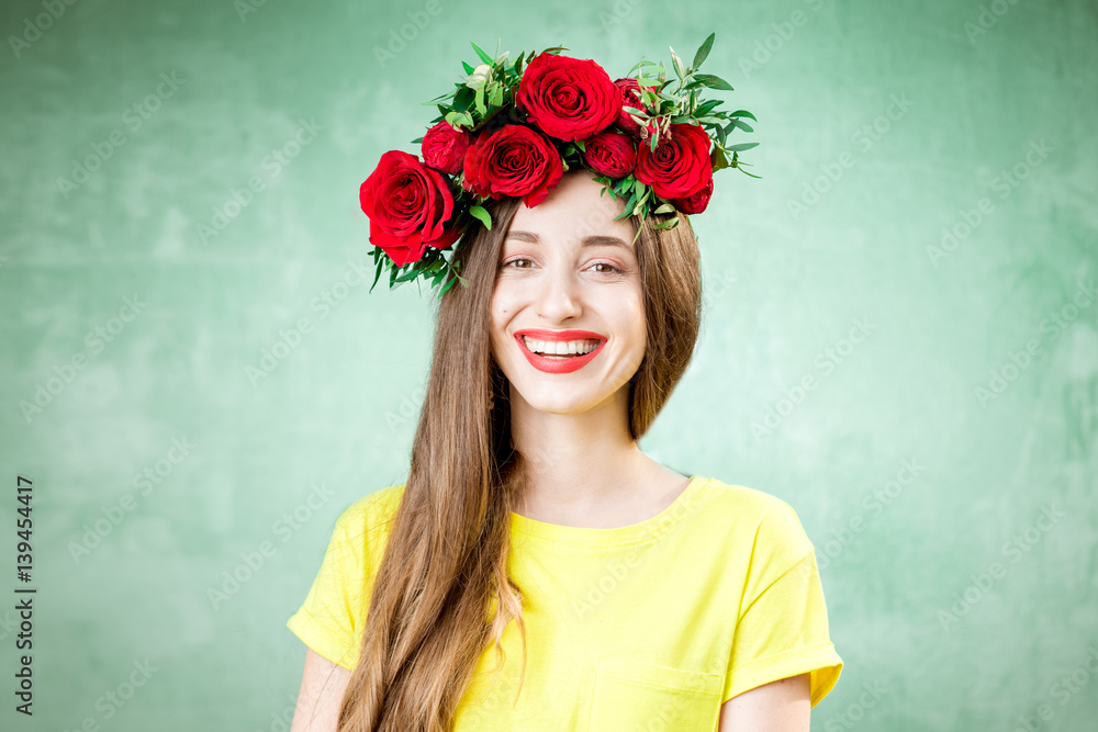 Colorful portrait of a beautiful woman in yellow t-shirt with wreath made of red roses on the green 