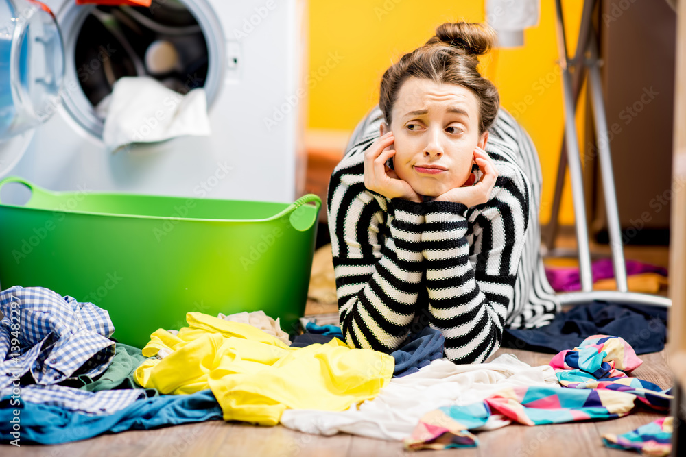 Tired housewife lying on the floor with lots of clothes near the washing machine at home